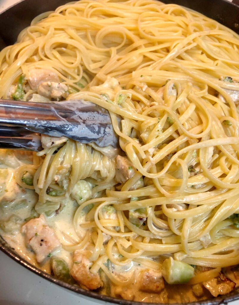 Using Tongs to Mix Pasta with Chicken Vegetables and Alfredo Sauce